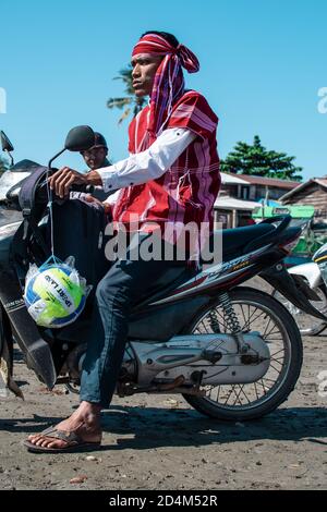 Chaung Thar, Myanmar - 26. Dezember 2019: Ein Einheimischer, der nicht mit einem Volleyball identifiziert wurde, sitzt am 26. Dezember 2019 in Chaung Thar auf einem Motorrad im Schlamm Stockfoto