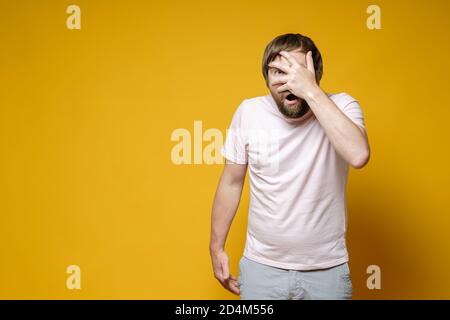 Erschrocken, überraschte Mann Gesicht mit der Hand bedeckt, öffnete Mund in Schock und schaute auf die Kamera mit einem Auge. Speicherplatz kopieren. Stockfoto