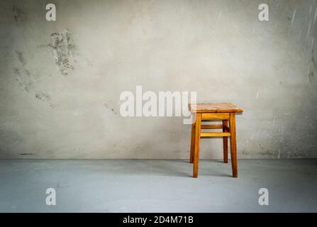 Holzhocker im leeren Raum. Stuhl auf Zementboden. Grunge Innenraum. Stockfoto