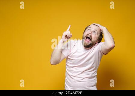 Seltsamer bärtiger Mann zeigt den Zeigefinger überraschenderweise nach oben, schreit aufgeregt und hält die Haare mit der Hand. Speicherplatz kopieren. Stockfoto