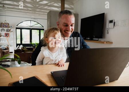 Vater und Tochter lachen zusammen über den Laptop und verbringen viel Zeit Stockfoto