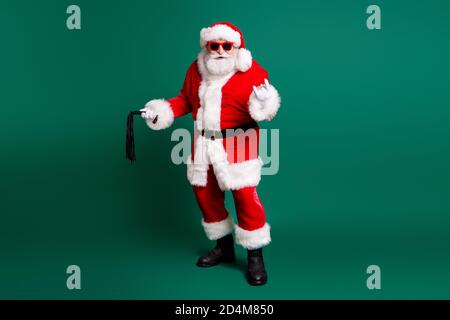 Volle Länge Körpergröße Ansicht seiner er schön Fett Übergewichtig cool bärtig Santa Vater hält in Händen Peitsche zeigen Horn Symbol genießen festliche Freizeit Stockfoto