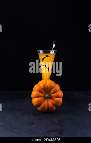 Oranger Kürbis und Kürbis alkoholfreier Mocktail in hohem Glas verziert Mit Papierfledermäusen und mit Papier gestreiftem Stroh und weiter Schwarze strukturierte Steinlasche Stockfoto