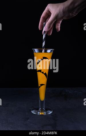 Frau Hand Putting Papier Stroh in Glas mit Kürbis alkoholfrei Mocktail verziert mit Papier Fledermäuse und steht auf schwarz strukturiert Steintisch Surfa Stockfoto