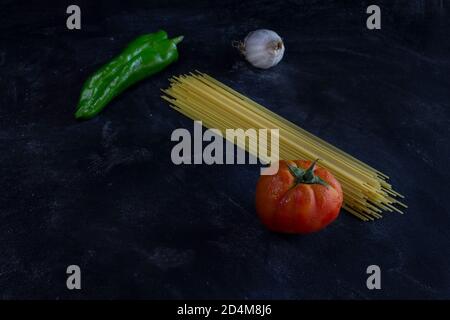 Draufsicht auf Pasta-Hintergrund mit Spaghetti, grünen Pfeffer, Tomaten und Knoblauch auf mehligen dunklen Hintergrund mit Kopieplatz für Text.Healthy Food Konzept. Stockfoto