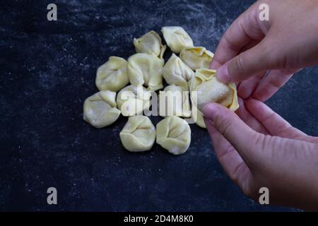 Hand hält frische Ravioli auf mehligen dunklen Hintergrund. Italienisches hausgemachtes gesundes Essen Konzept. Stockfoto