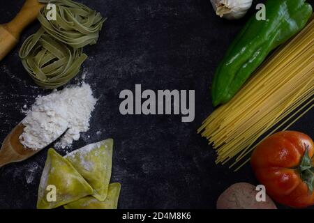 Food Hintergrund mit Spaghetti, Ravioli, grüner Pfeffer, Zwiebel, Kartoffel und Knoblauch auf mehligen dunklen background.Healthy hausgemachte Küche concept.Copy Raum, p Stockfoto
