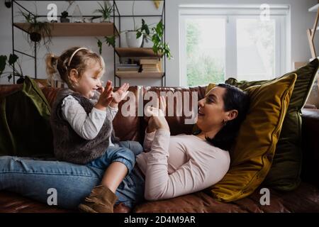 Kaukasische Mutter und Tochter spielen zu Hause auf dem Sofa, kitzeln und lachen Stockfoto