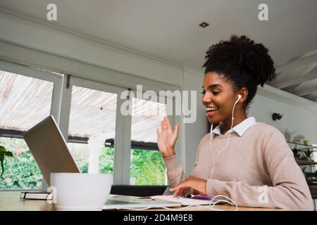 Glückliche afroamerikanische Geschäftsfrau chatten auf Videoabruf von Laptop sitzen mit heißem Kaffee in der modernen Küche. Stockfoto