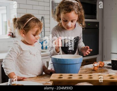 Junge kaukasische Schwestern backen zusammen in der Küche, machen ein Chaos und Spaß haben Stockfoto