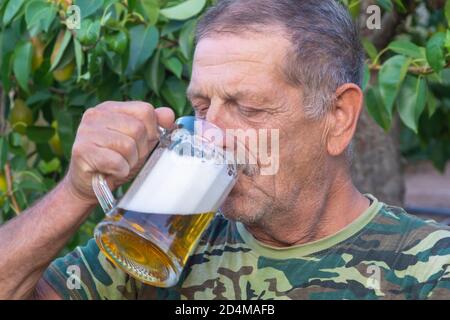 Senior Mann trinkt Bier mit Schaum aus einem Becher im Freien. Entspannung und Alkoholkonzept, selektiver Fokus, Nahaufnahme. Stockfoto