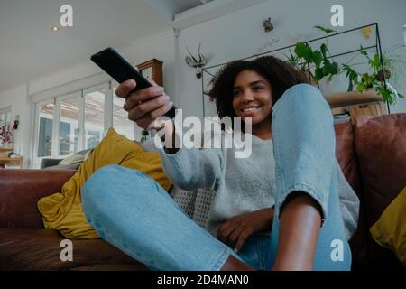 Frau mit gemischter Rasse, die die Fernbedienung auf der Couch hält. Stockfoto