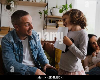 Tochter zeigt Papa fertig Hausaufgaben lächelnd auf einander im Wohnzimmer stehen. Stockfoto