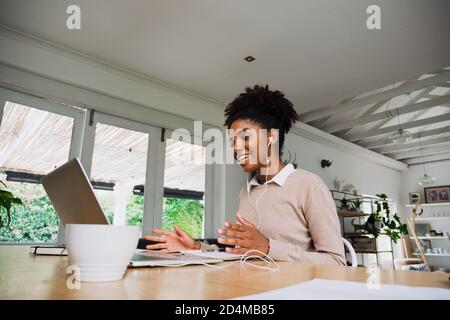 Lächelnde Geschäftsfrau trägt Kopfhörer und chattet mit einem Videoanruf auf dem Laptop und Kaffee in der modernen Küche. Stockfoto