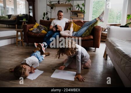 Junge kaukasische Familie genießen gemeinsame Zeit in der Lounge, Eltern auf dem Smartphone, während Tochter zeichnen Stockfoto