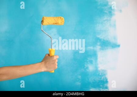 Nahaufnahme der weiblichen Hand halten Farbe gelb Rolle über blauen Hintergrund-Reparatur-, Bau-und Bauwerkzeuge Konzept. Praktisch und vielseitig Stockfoto