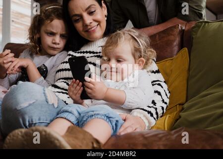 Mutter und zwei Töchter beobachten lustige Videos auf dem Smartphone sitzen auf dem Sofa in der modernen Lounge. Stockfoto