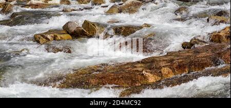Die Sonne scheint auf dem schnellen Quellfluss, der über braune Felsen fließt, breites Banner Stockfoto