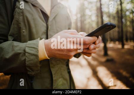 Junge kaukasische männliche SMS auf Smartphone, während im erdigen Wald stehen. Stockfoto
