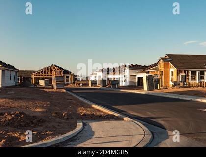 Eine Reihe neuer Häuser, die während des Baubooms in Arizona gebaut werden, steht im frühen Morgenlicht auf einem unbefestigten Grundstück, horizontale Ansicht. Stockfoto