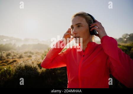 Kaukasische Sportlerin, die beim Laufen im Wald Musik mit Kopfhörern hört. Stockfoto