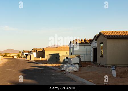 Eine Reihe neuer Häuser, die während des aktuellen Baubooms im Südwesten der USA gebaut werden, steht im frühen Morgenlicht auf einem unbefestigten Grundstück, horizontale Ansicht. Stockfoto
