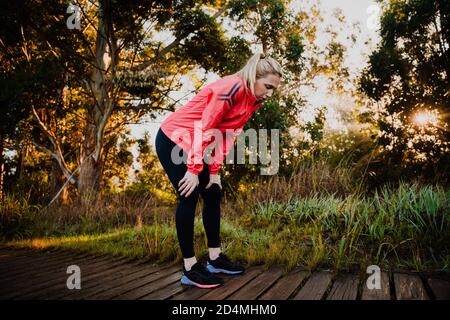 Athletische Frau müde vom Laufen im Park, gebogen über Atmung schwer Stockfoto