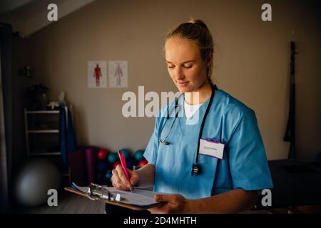 Porträt der kaukasischen Ärztin in Scrubs mit Zwischenablage und Checkliste Stockfoto