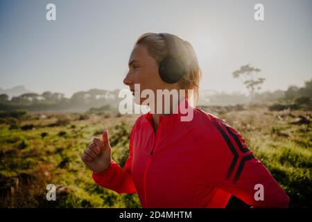 Athletische kaukasische Frau, die im Freien läuft und Musik mit Kopfhörern hört. Stockfoto