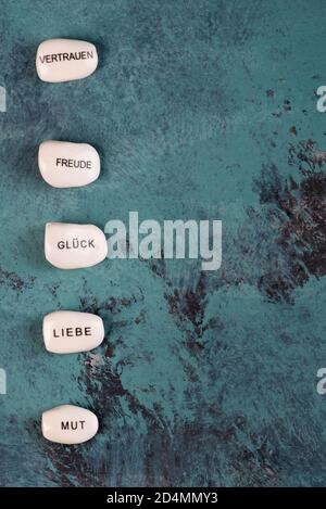Weißer Stein mit deutschen Worten Liebe, Vertrauen, Mut, Glück, Spaß auf blauem texturierten Hintergrund, leerer Platz für Text Stockfoto
