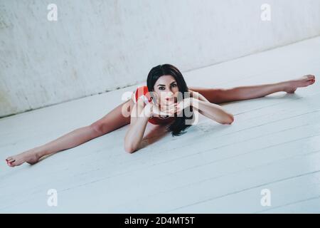 Junge Brünette Fitness Frau Stretching Beine in weißen Raum Interieur Stockfoto
