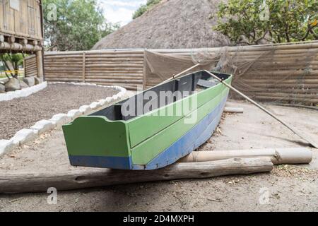 Kleines grünes und blaues Holzboot mit Rudern, auf einigen Holzpfosten, neben einem Pfad mit weißen Steinen, Details Stockfoto