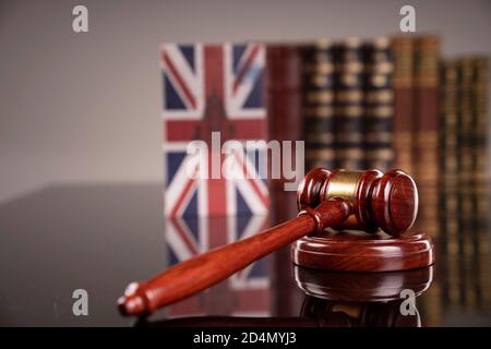 Thema „Recht“. Richterkammer. Richtergavel, Union Jack Flagge und Sammlung von juristischen Büchern auf dem braunen Schreibtisch und dem braunen Hintergrund. Stockfoto