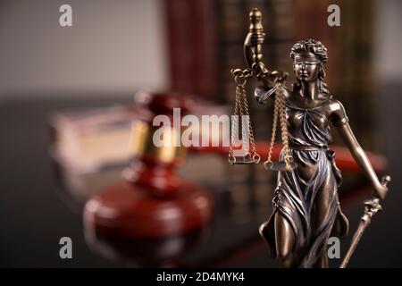 Thema „Recht“. Richterkammer. Richtergavel, Themis Statue und Sammlung von juristischen Büchern auf dem braunen Schreibtisch und dem braunen Hintergrund. Stockfoto