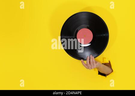 Weibliche Hand hält Vinyl Record durch eingerissene Loch in gelber Papierwand. Minimalistisches Retro-Konzept Stockfoto