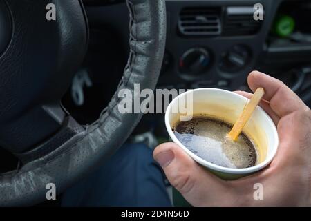 Papiertasse Kaffee in der Hand des Fahrers am Rad des Autos Stockfoto