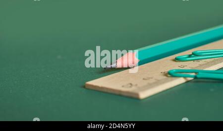 Ein einfacher Bleistift, ein Holzlineal und zwei Büroklammern liegen auf einem schlichten grünen Hintergrund. Nahaufnahme. Makro Stockfoto