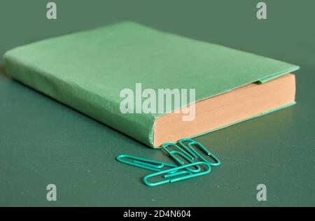 Ein grün bedecktes Buch und Büroklammern liegen auf einem schlichten grünen Hintergrund. Nahaufnahme Stockfoto