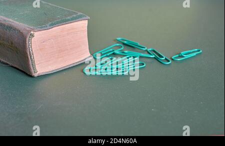 Ein grün bedecktes Buch und Büroklammern liegen auf einem schlichten grünen Hintergrund. Nahaufnahme Stockfoto