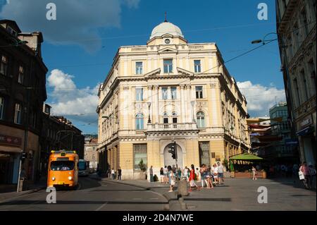 Eine Straßenbahn auf der Straße neben der Ewigen Flamme, ein Denkmal für die militärischen und zivilen Opfer des Zweiten Weltkriegs in Sarajevo. Stockfoto