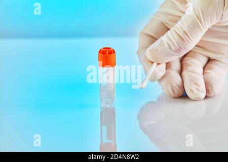 DNA-Test. Reagenzglas mit Flüssigkeit für DNA-Analyse und einer Handschuhen mit einem Stick auf blauem Hintergrund mit Reflexion. Stockfoto