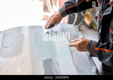 Reparatur Karosserie, Anwendung Kitt Nahaufnahme. Der Mechaniker repariert das Auto. Arbeiten Sie nach dem Unfall mit Schleifgrundierung vor dem Lackieren. Stockfoto