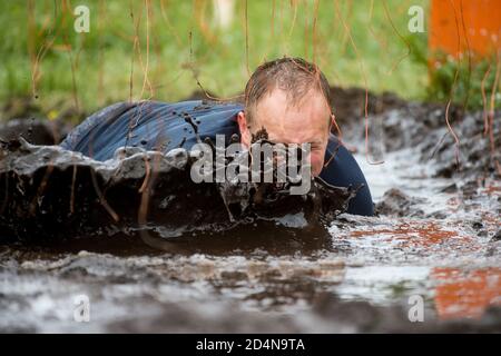 Schlammläufer. Krabbeln, unter einem Stacheldraht Hindernisse während extremer Hindernis Rennen passieren. Extremes Sportkonzept Stockfoto