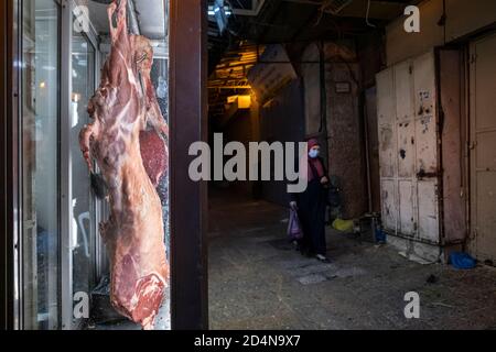 Eine Palästinenserin, die wegen der COVID-19-Coronavirus-Pandemie eine Gesichtsmaske trägt, geht an einer Metzgerei in der Altstadt des muslimischen Viertels, Ostjerusalem, Israel, vorbei Stockfoto