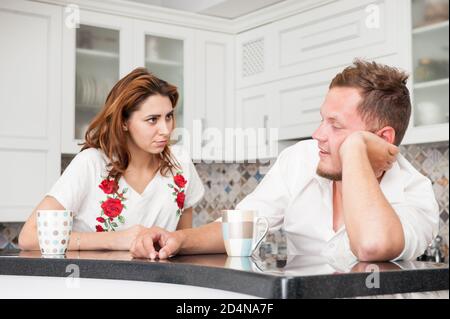 Wütend junge hübsche Frau und glücklich betrunken Mann sitzen mit Tassen Tee in der Küche Stockfoto