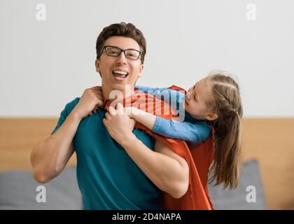 Vater und sein Kind spielen zusammen. Mädchen und Vater im Superhelden Kostüm. Papa und Kind haben Spaß, lächeln und umarmen. Familienurlaub und Zweisamkeit Stockfoto