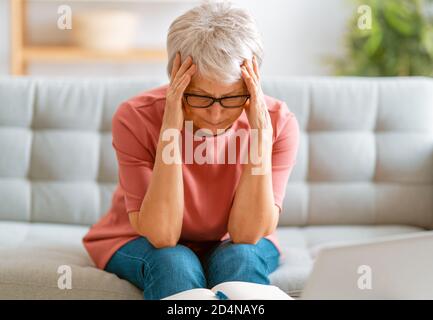 Ältere erschöpfte Frau, die zu Hause auf dem Sofa sitzt. Stockfoto