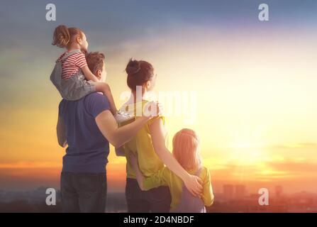 Glückliche Familie bei Sonnenuntergang. Vater, Mutter und zwei Kinder Töchter Spaß und Spiel in der Natur. Das Kind sitzt auf den Schultern seines Vaters. Stockfoto