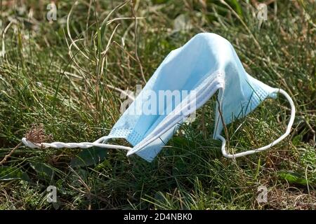 Gebrauchte blaue Gesichtsmaske auf dem Boden im Gras. Gesichtsmaske ist falsch entsorgt. Umweltverschmutzung und Umweltkatastrophe. Covid-19 Pandemie Stockfoto