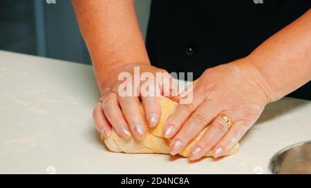 Nahaufnahme der Hände, die ein großes Stück Gebäck, die Herstellung von Buns aus Teig. Älterer Bäcker im Ruhestand mit bonete Zutaten mischen mit gesiebenem Weizenmehl Kneten zum Backen von traditionellen Kuchen und Brot. Stockfoto